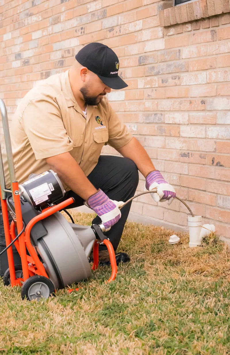 Mahi Plumbing plumber running a drain-cleaning machine at an outdoor sewer cleanout