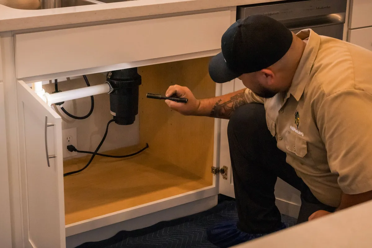 Mahi Plumbing plumber inspecting a garbage disposal inside an under-sink cabinet