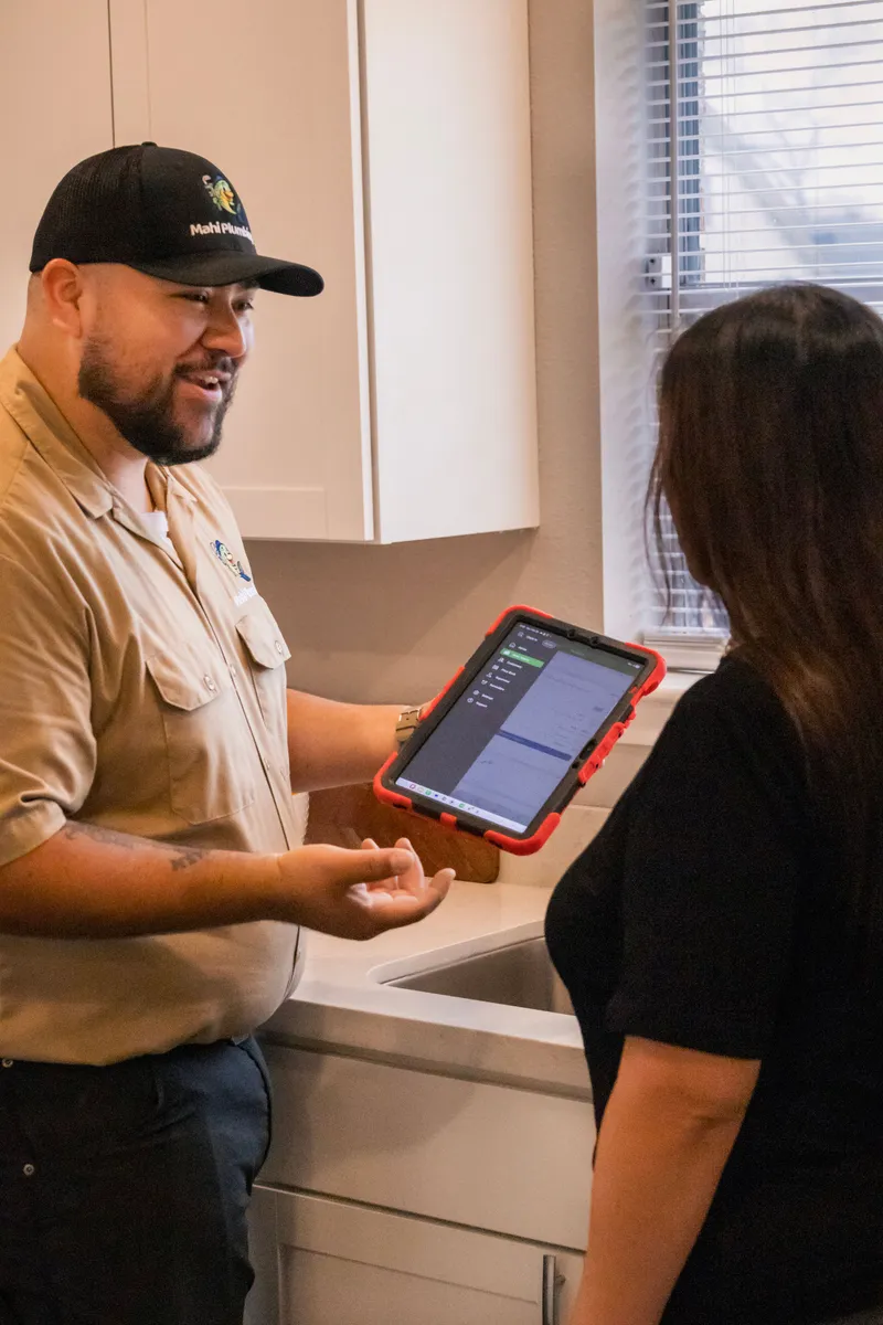 Mahi Plumbing owner reviewing an upfront flat-rate estimate on a tablet with a homeowner